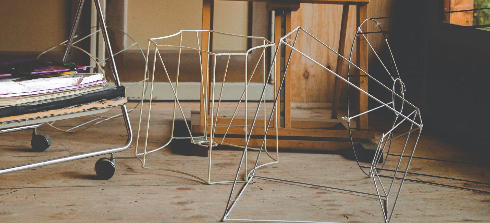 Draadframe sculpturen staan ​​op een houten vloer, vlakbij een kar en een houten deur.