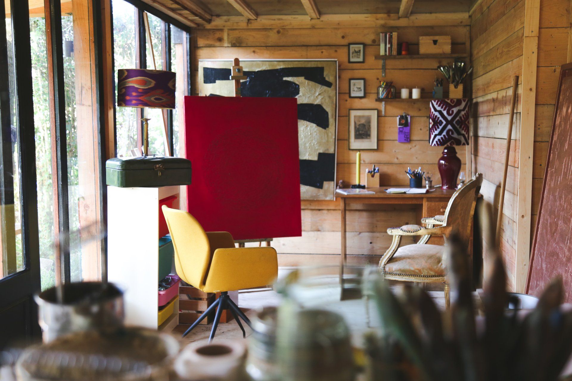Kunstenaarsatelier met rood canvas, gele stoel, houten wanden en kunstbenodigdheden.