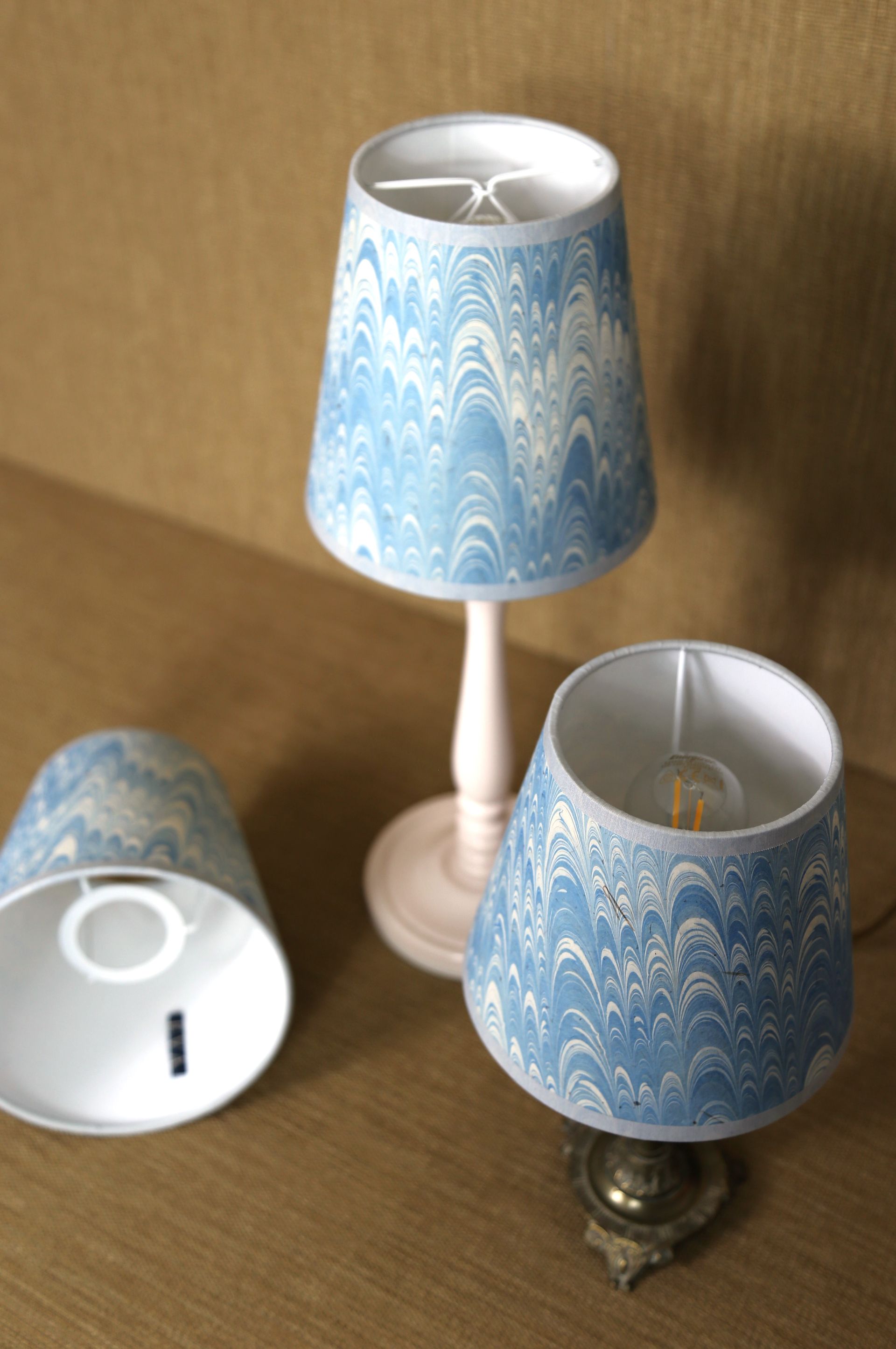 Drie kleine lampjes met blauw gemarmerde kappen op een houten ondergrond. Eén lampje brandt.
