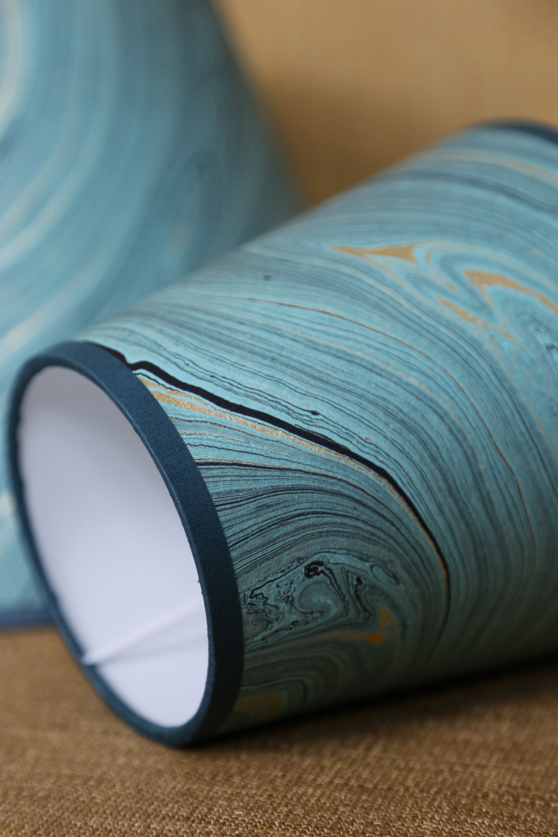 Twee lampenkappen van marmer in turquoise en goud, van dichtbij. Turquoise rand en witte binnenkant.