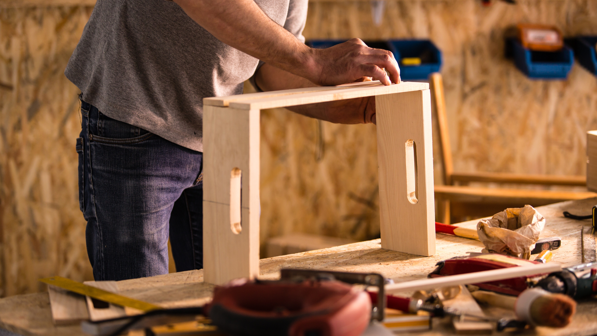 Man building a wooden stool with a workshop background.