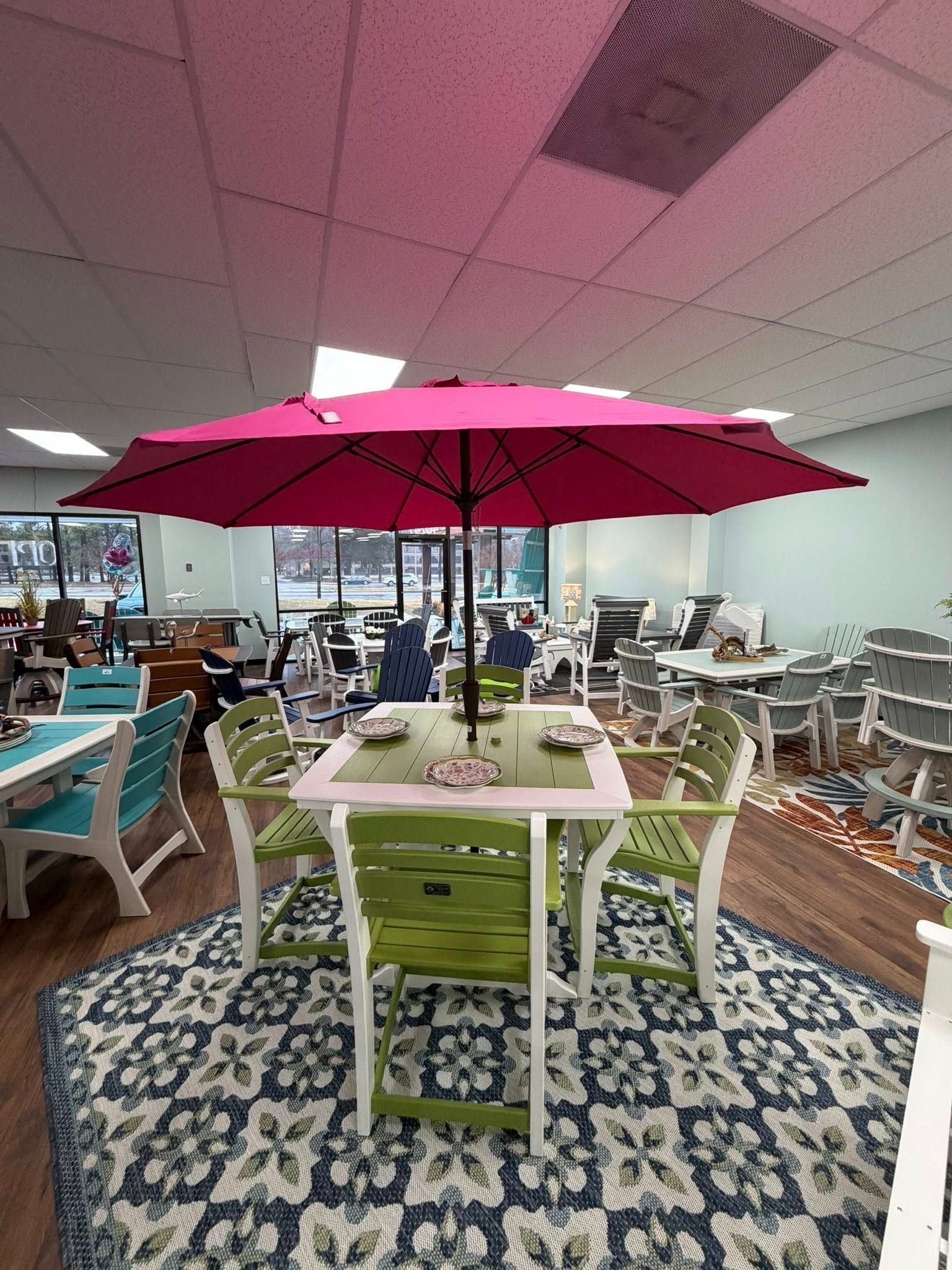 A patio set with a pink umbrella, a square table, and green chairs on a patterned rug.