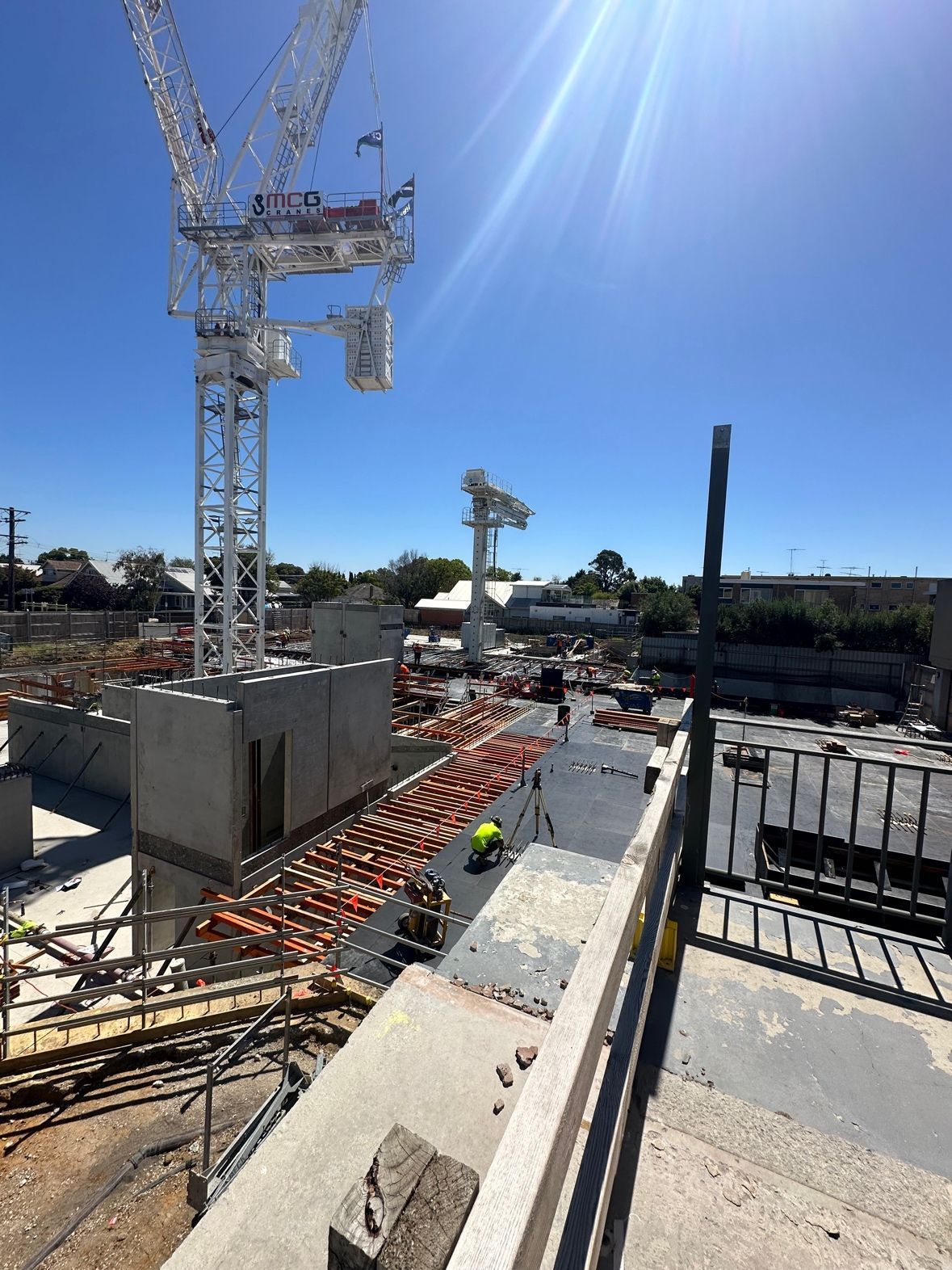 Construction site with two cranes under a bright blue sky. Workers are laying orange bricks.