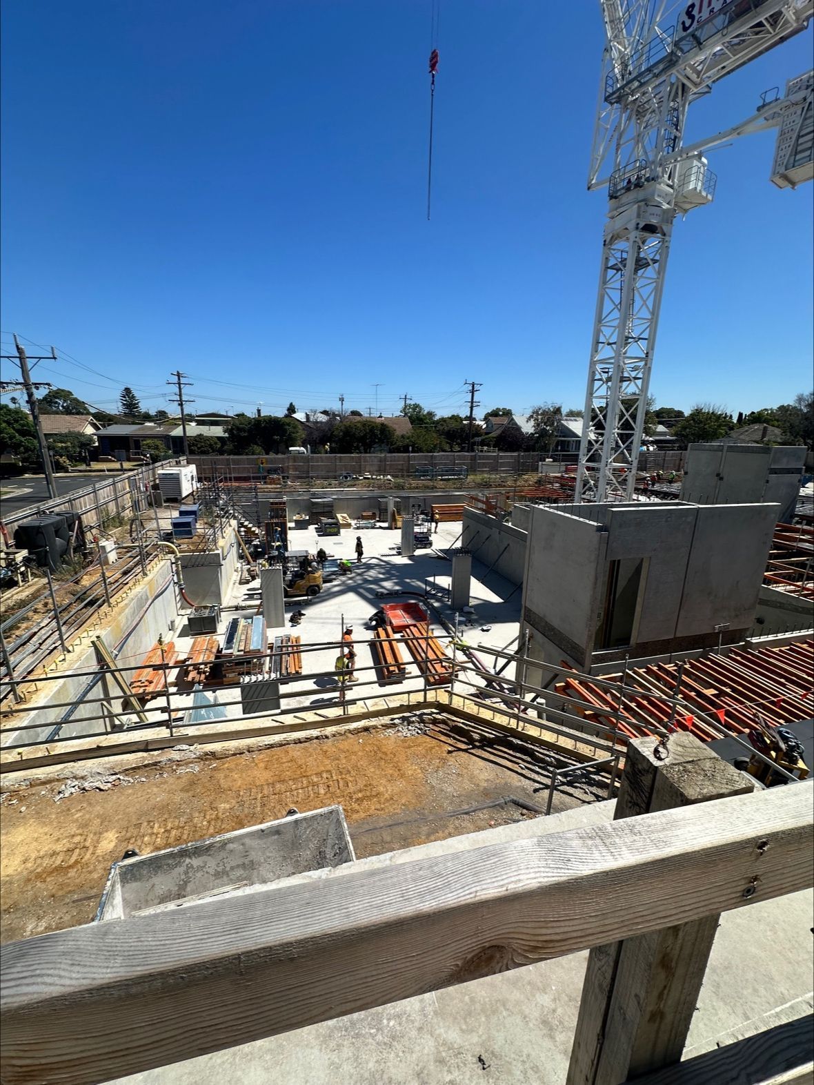 Construction site with crane, concrete foundation, and building materials on a sunny day.