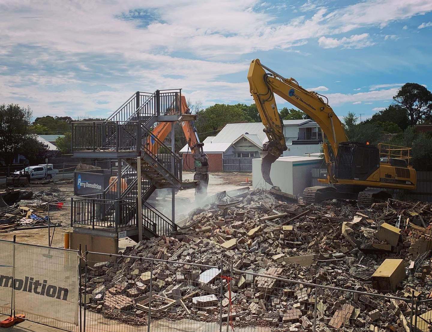 Construction site with two excavators demolishing a building; debris everywhere.