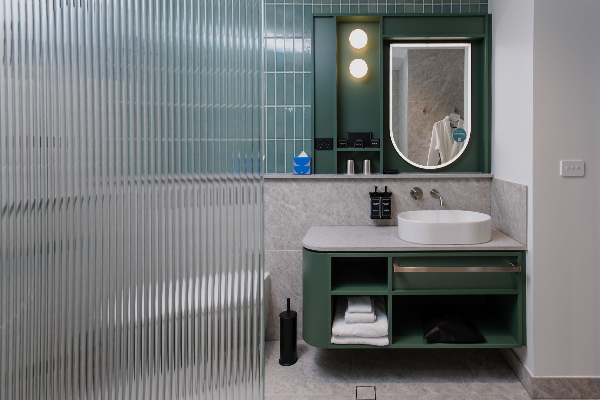 Green and white bathroom with a marble sink, fluted glass shower screen, and dark green cabinetry.
