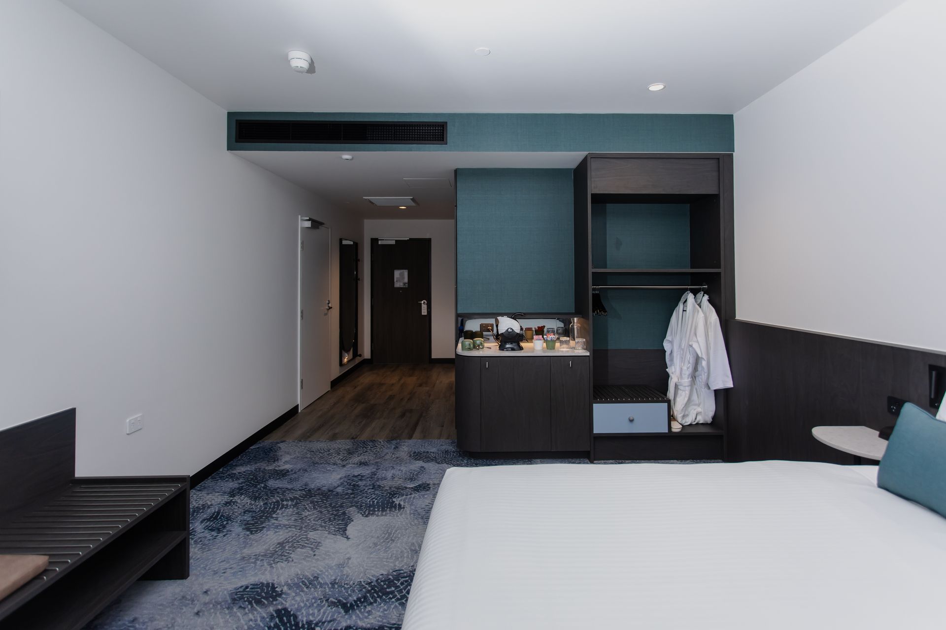 Hotel room with bed, wardrobe, and door. Teal accent wall, white walls, and patterned carpet.