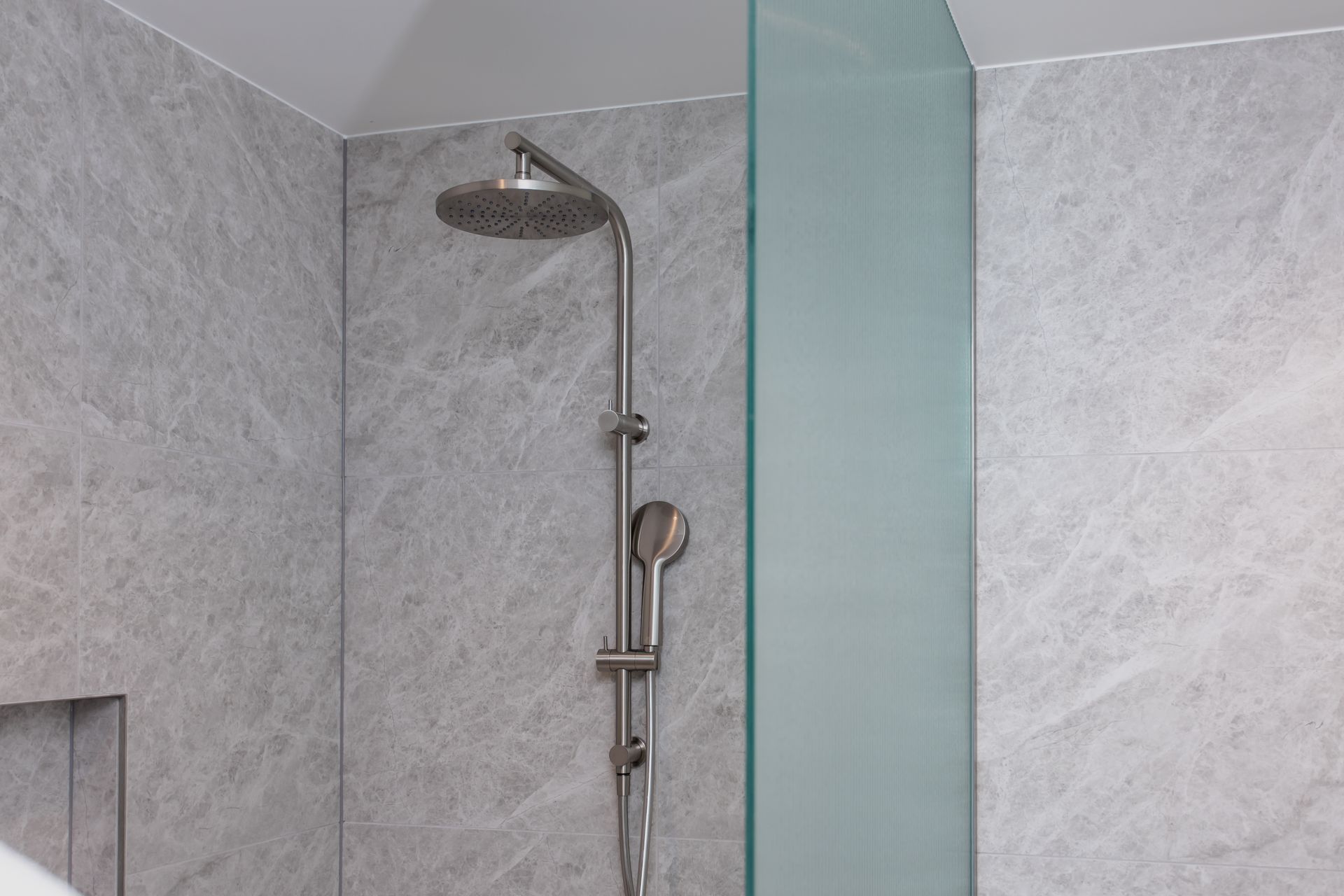 Shower with a large rain shower head and handheld nozzle against gray stone tile, with a glass wall.