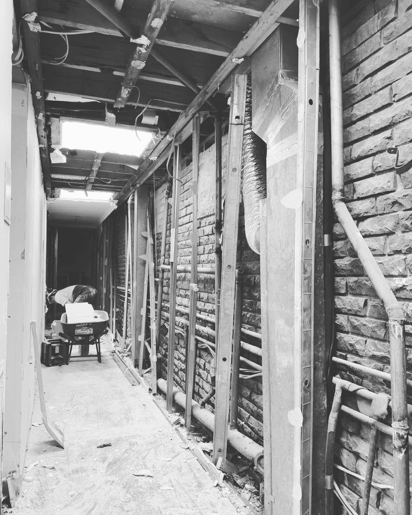 Narrow hallway under construction; exposed brick, wooden framing, partial ceiling, and tools.