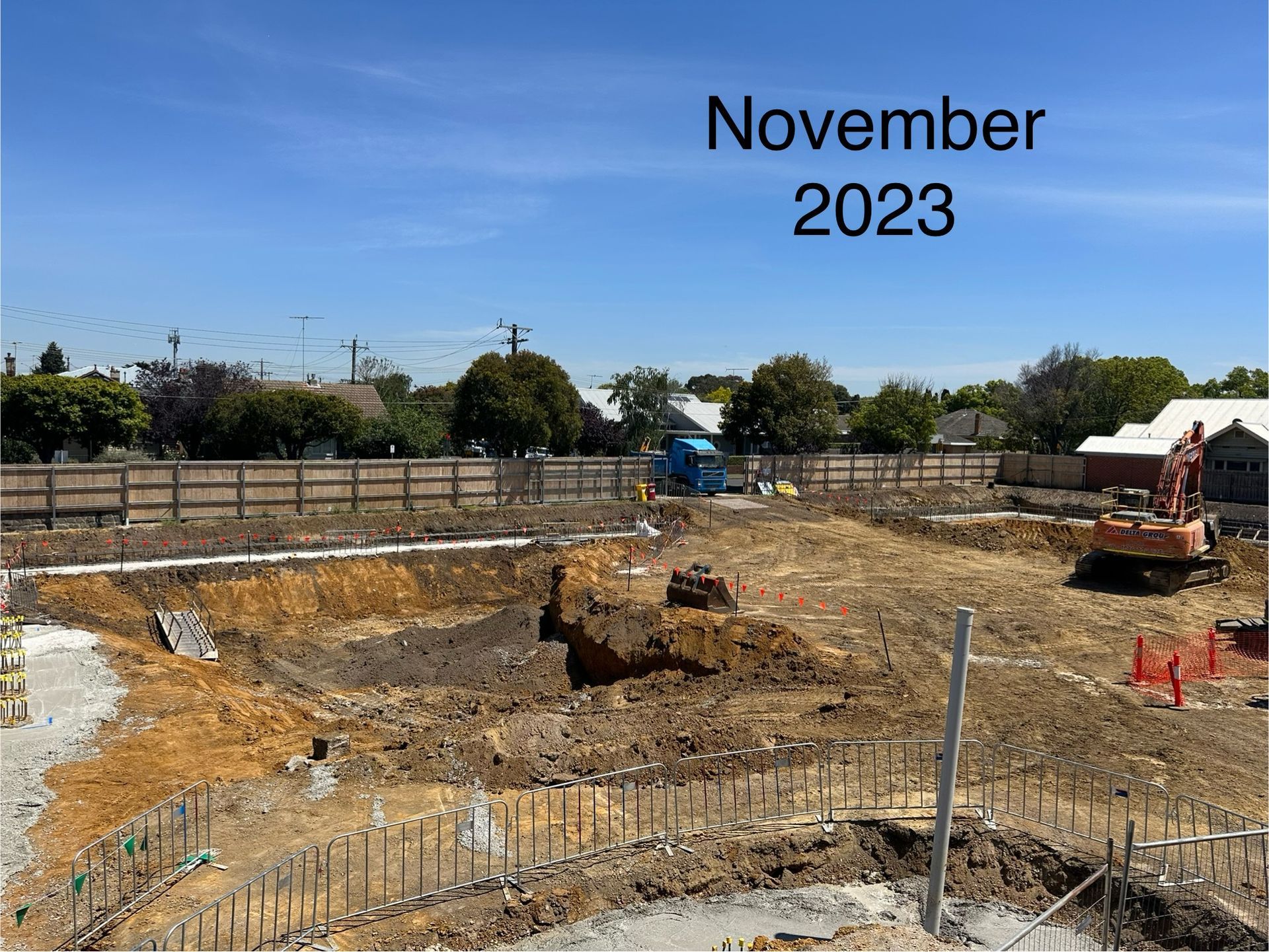 Construction site in November 2023. Excavated earth, equipment, and a partially-built foundation are visible under a blue sky.