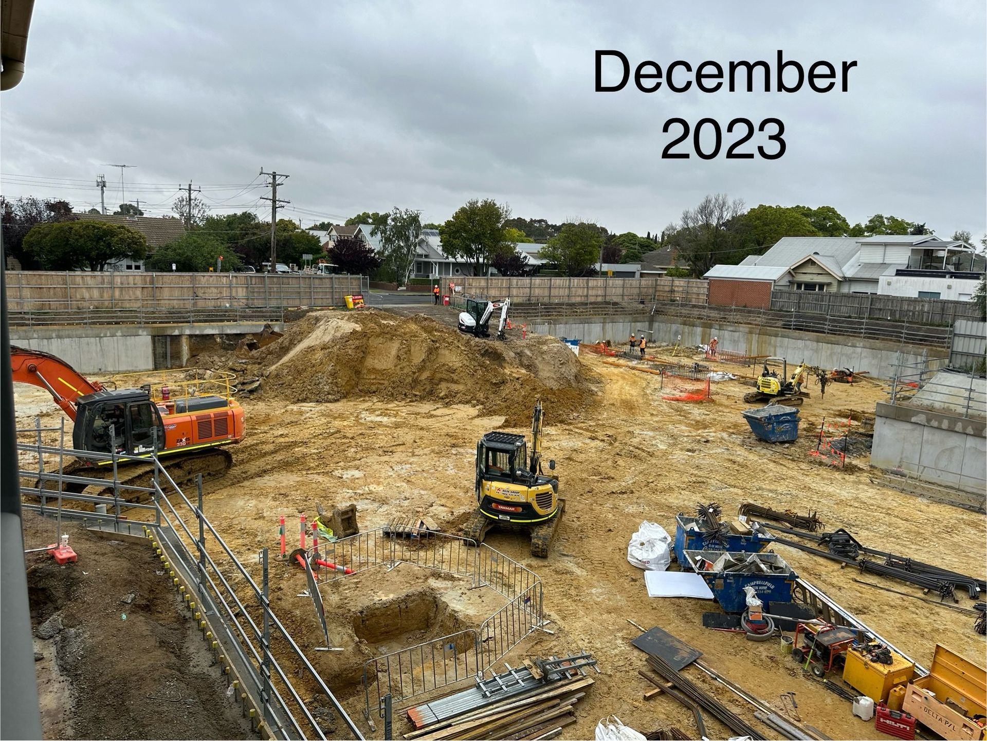 Construction site in December 2023. Heavy machinery on dirt ground, fenced perimeter, overcast sky.
