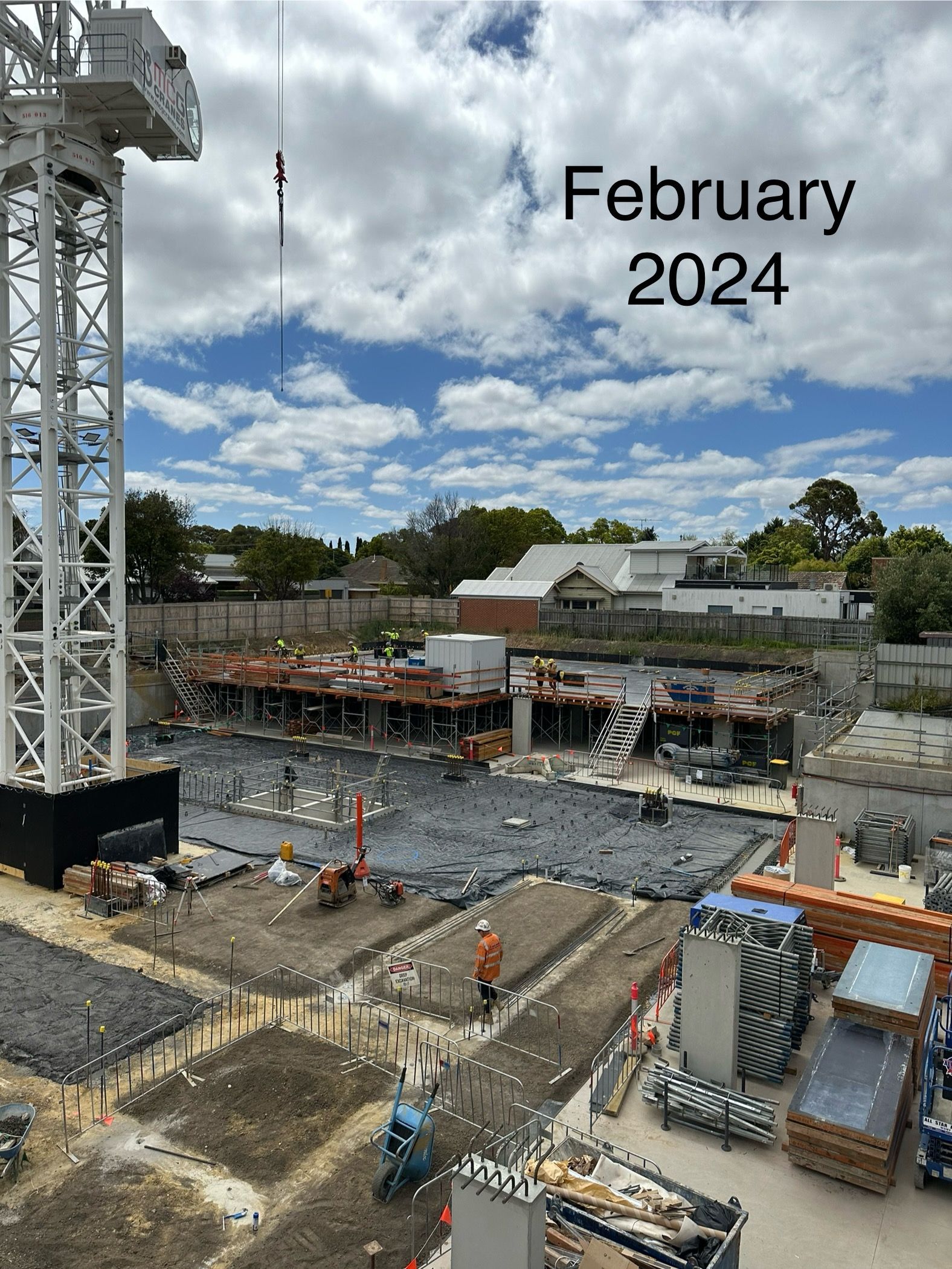Construction site in February 2024; crane, buildings under construction, workers, blue sky with clouds.