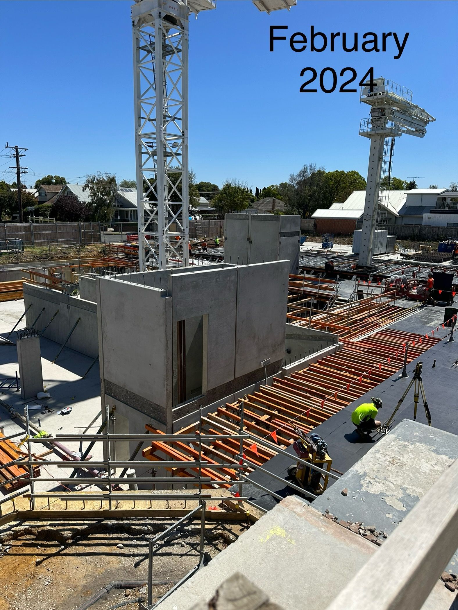 Construction site with crane, concrete walls, scaffolding, and workers. Sunny day, blue sky.