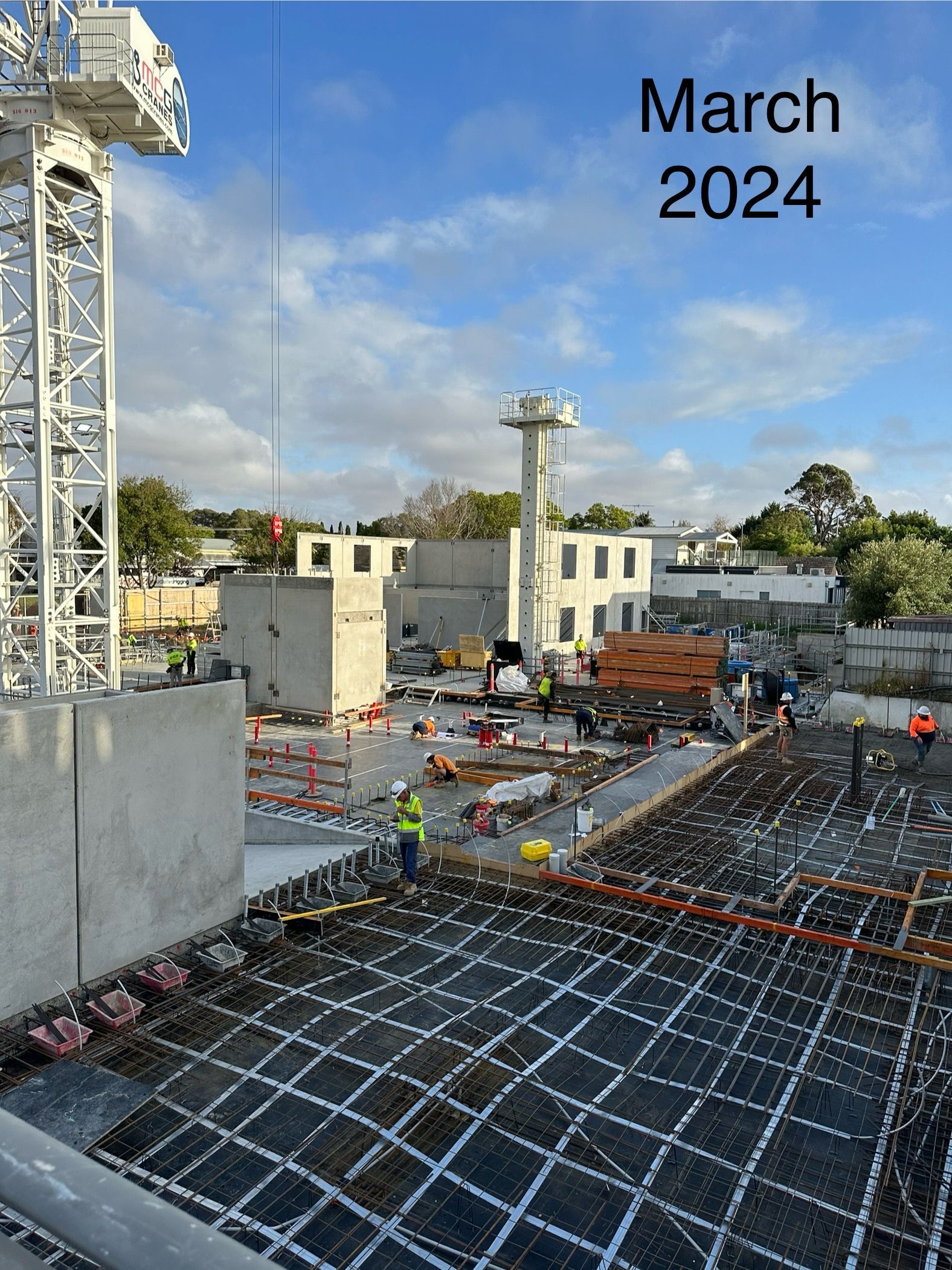 Construction site, March 2024, workers, crane, concrete, rebar, blue sky.