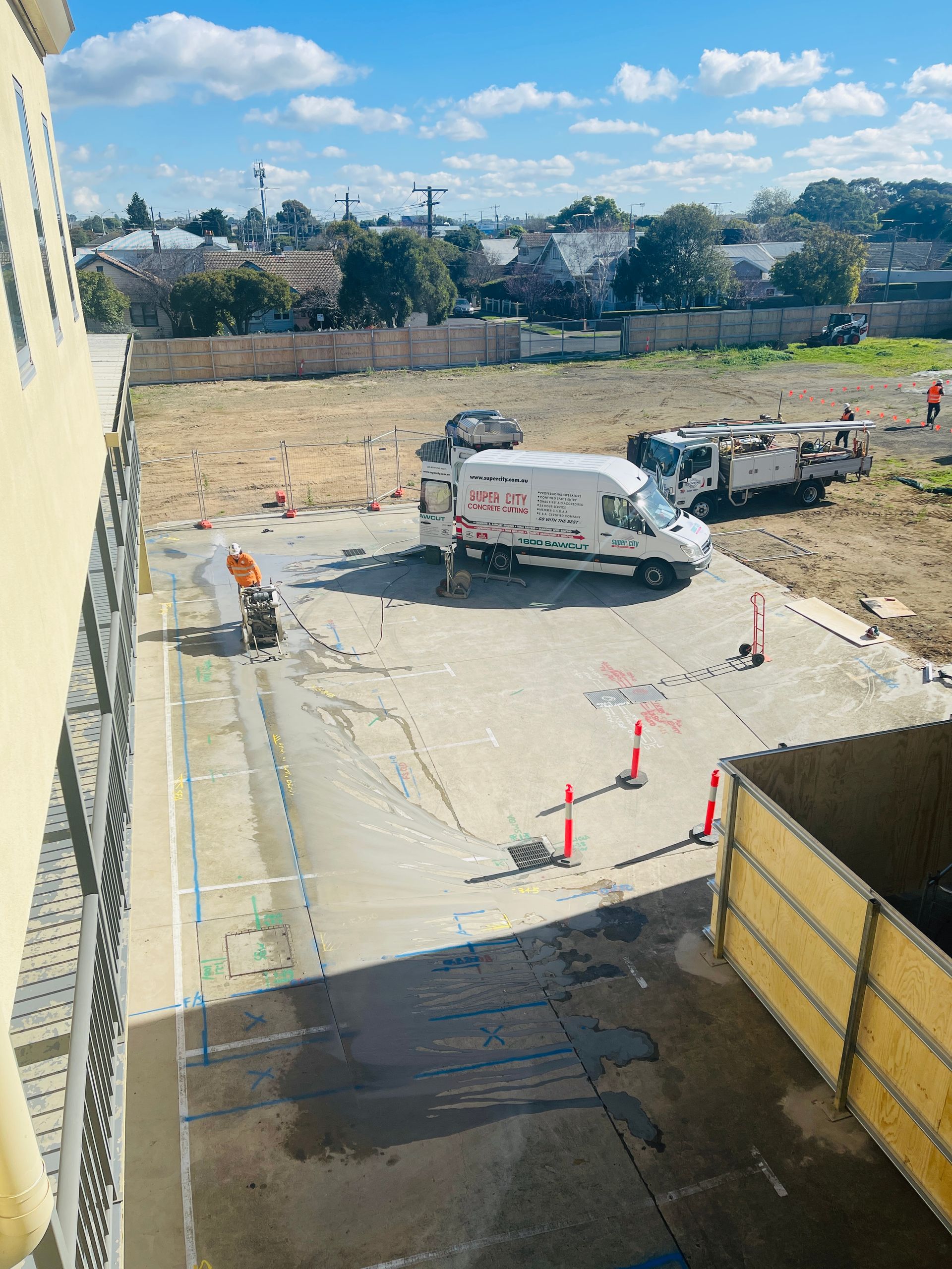 Construction site with vehicles and workers, open area with buildings in the background.