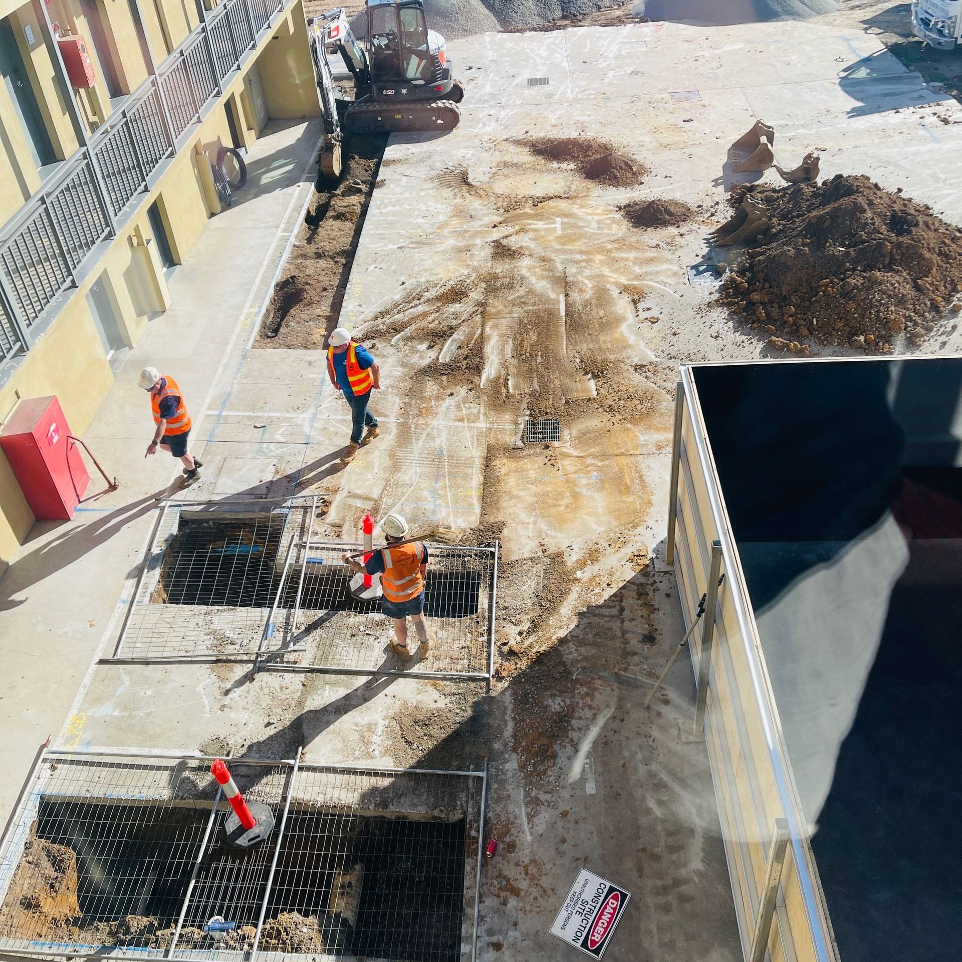 Construction workers in orange vests digging in a paved area near a building.