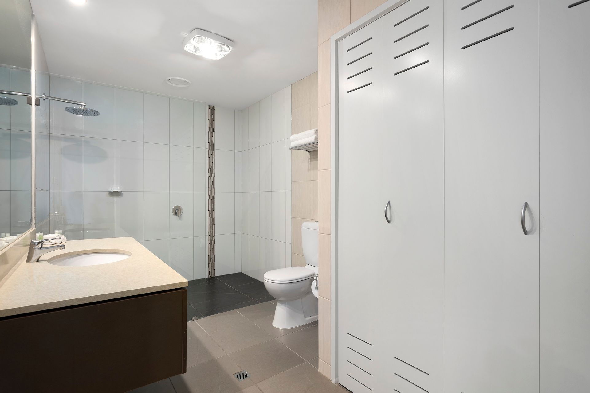 Bathroom with white cabinets, sink, toilet, and shower. Gray and brown accents.
