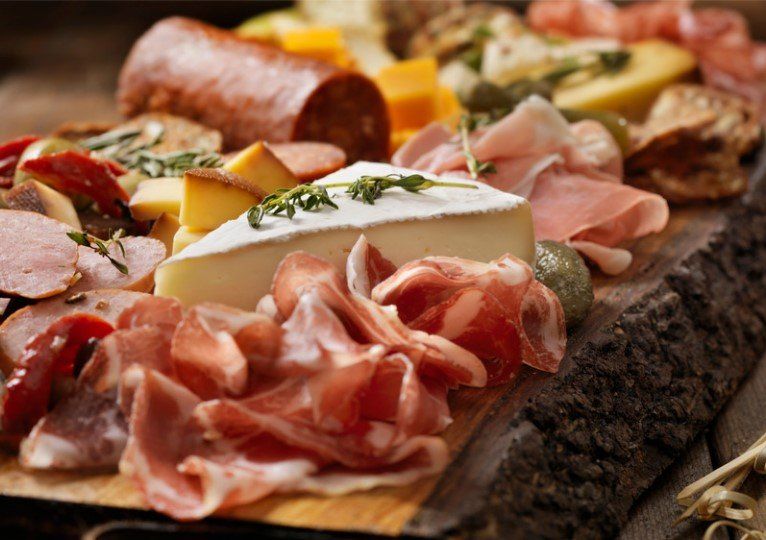 Charcuterie board with meats, cheeses, and olives, arranged on a wooden serving board.