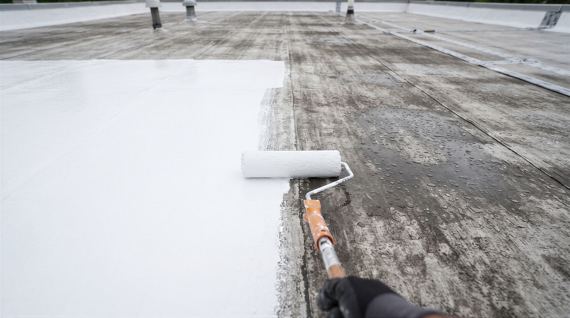 Worker applying white reflective roof coating on a flat commercial roof