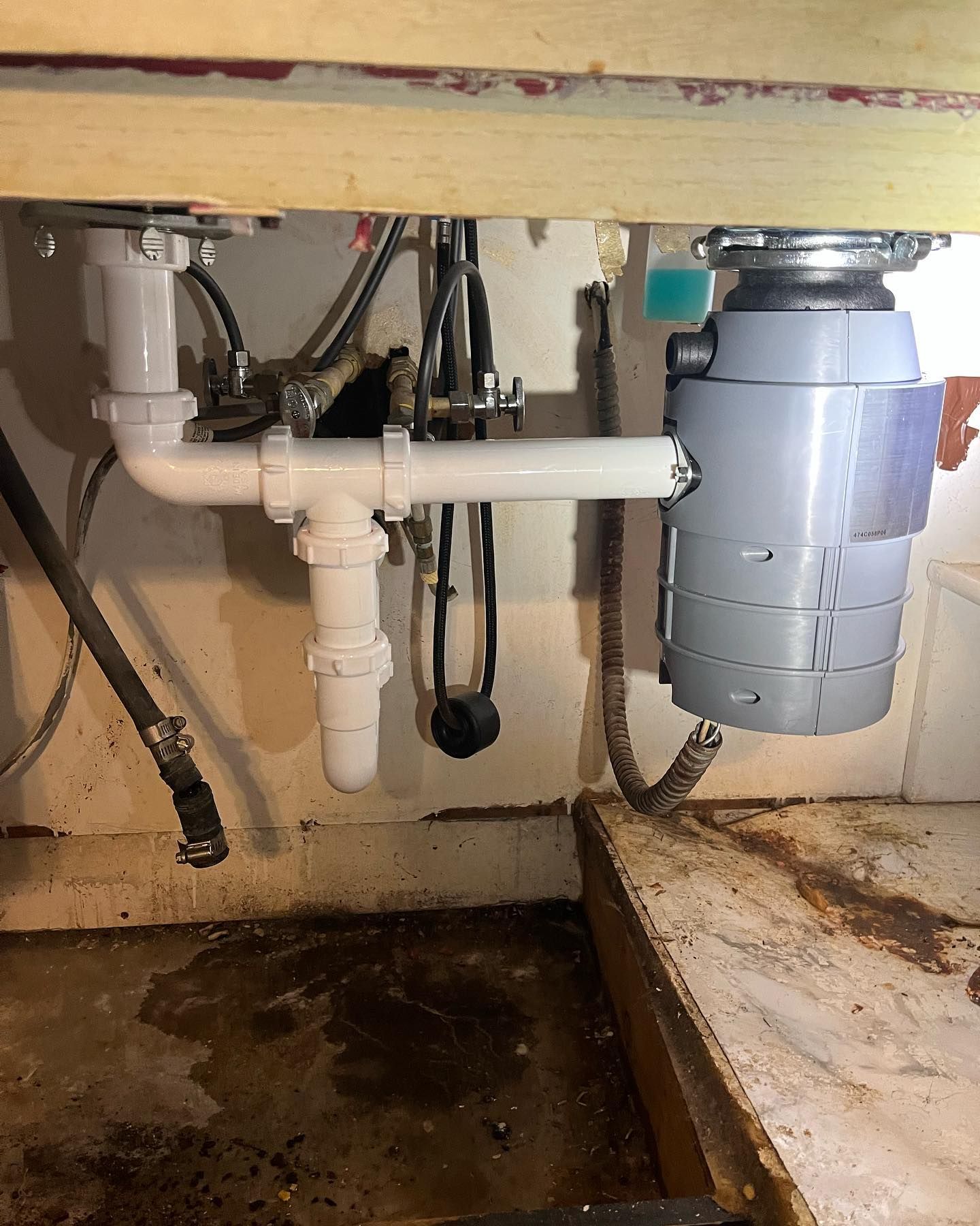 Under-sink view showing a garbage disposal connected to a white PVC pipe drainage system in a cabinet.