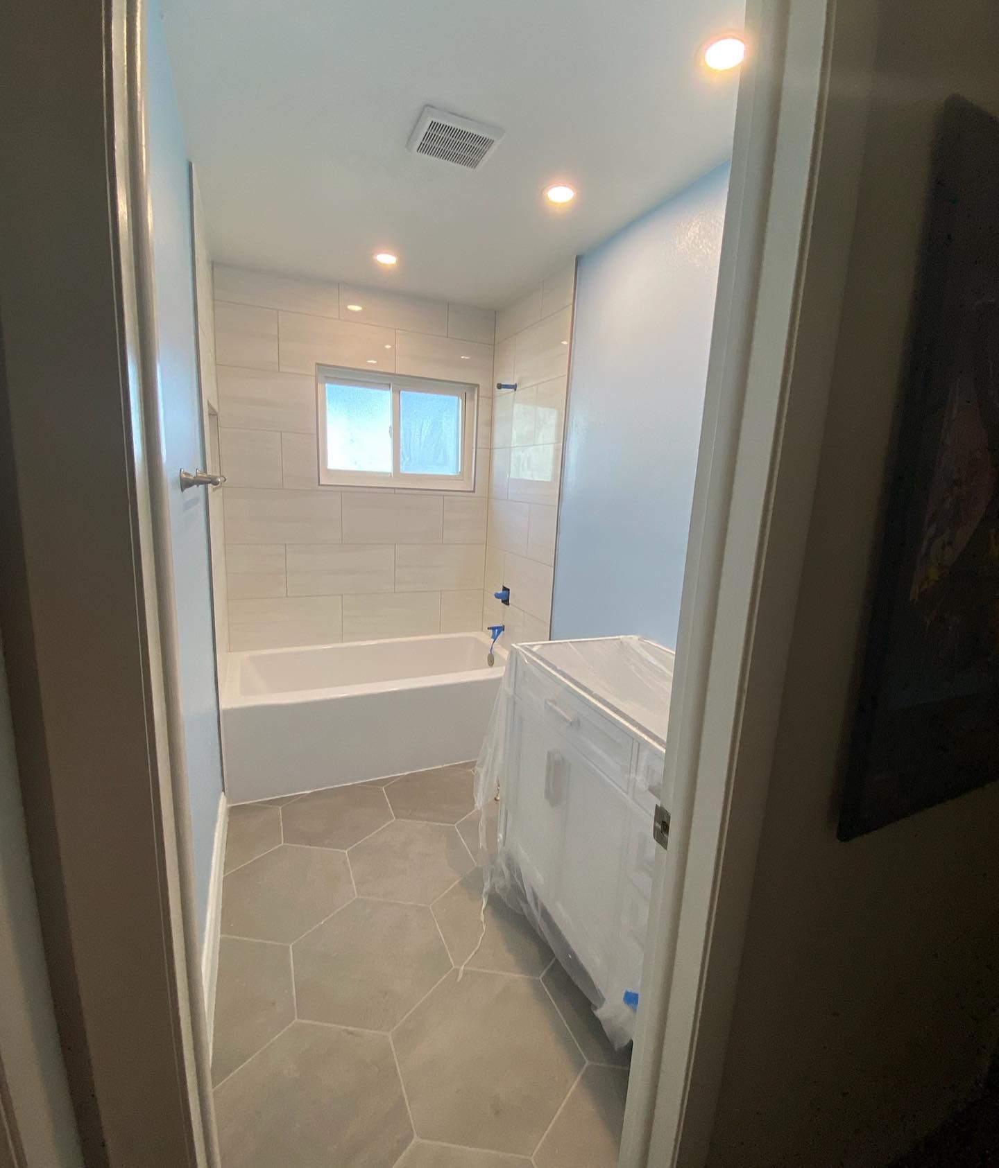 A renovated bathroom with gray hexagonal floor tiles, a white bathtub with subway-style tiles, and a new vanity.