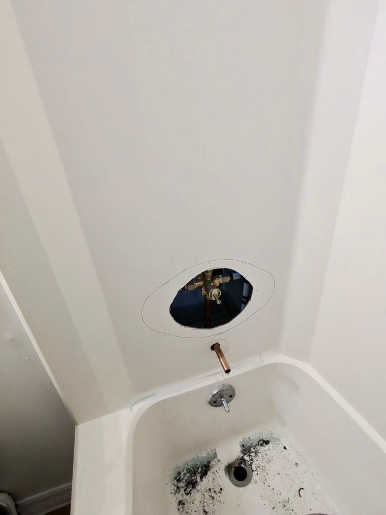 A hole cut in a white shower wall surrounding the faucet plumbing, with a shower head pipe protruding below it.