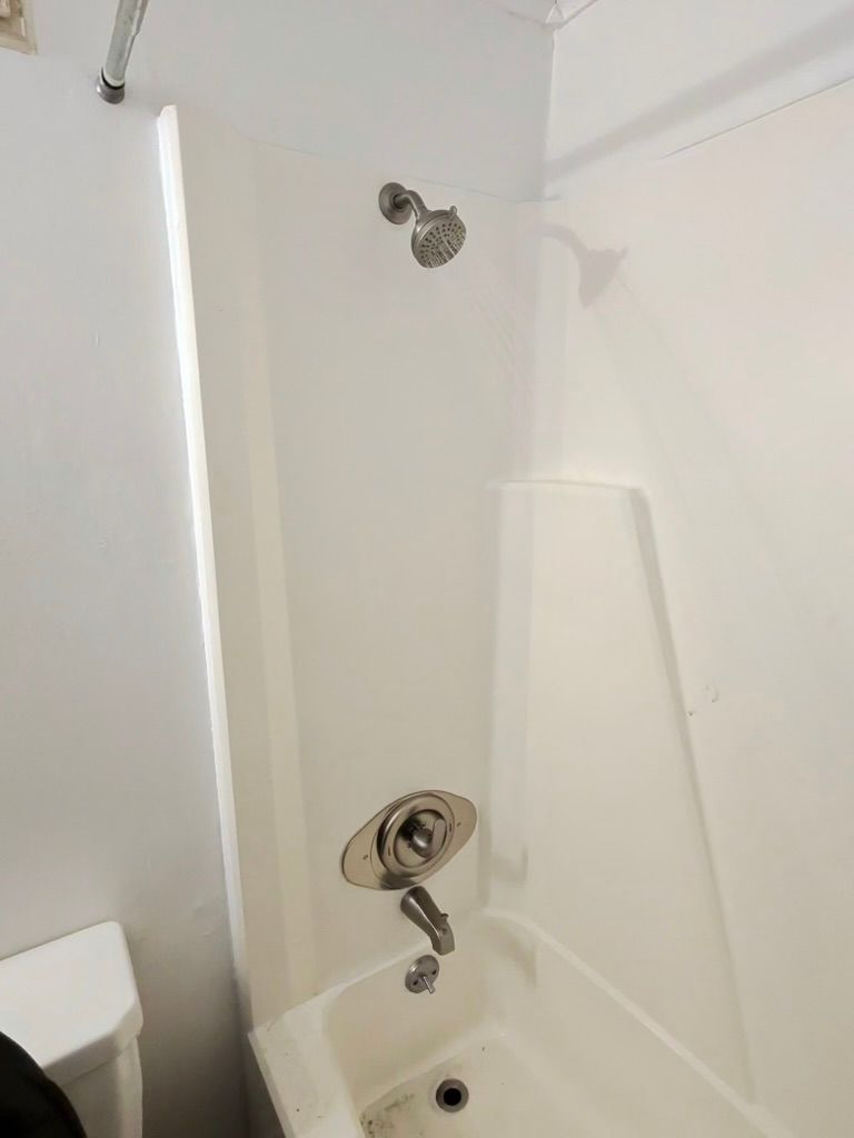 A white bathtub and shower surround with a chrome showerhead and faucet handle.