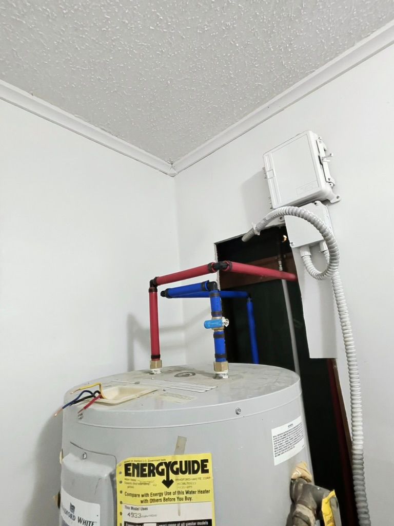 Water heater with blue and red piping, an EnergyGuide label, and a wall-mounted electrical box in a corner.