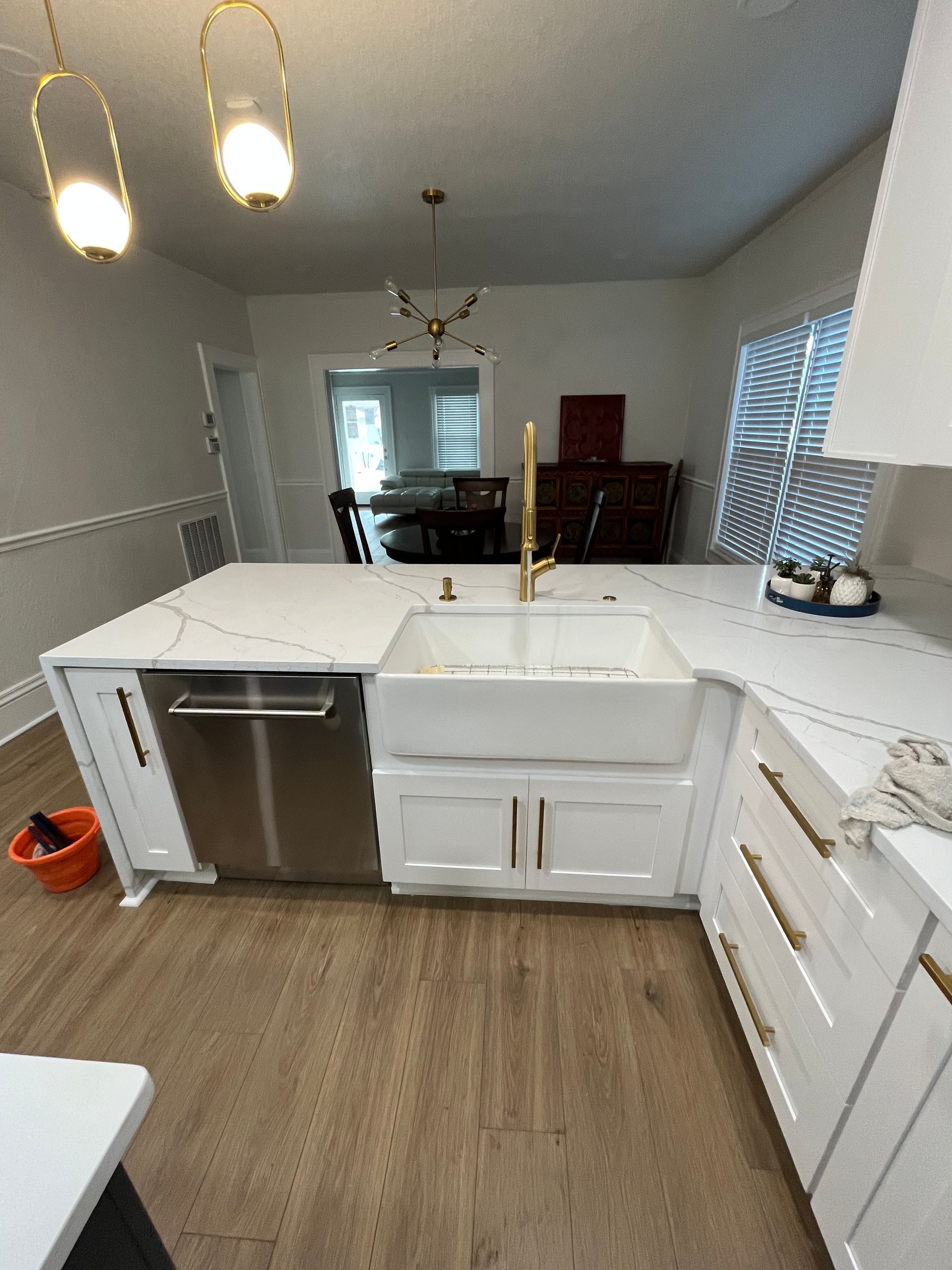 A modern kitchen featuring white cabinets, a farmhouse sink, gold hardware, and marble countertops with gold veining.