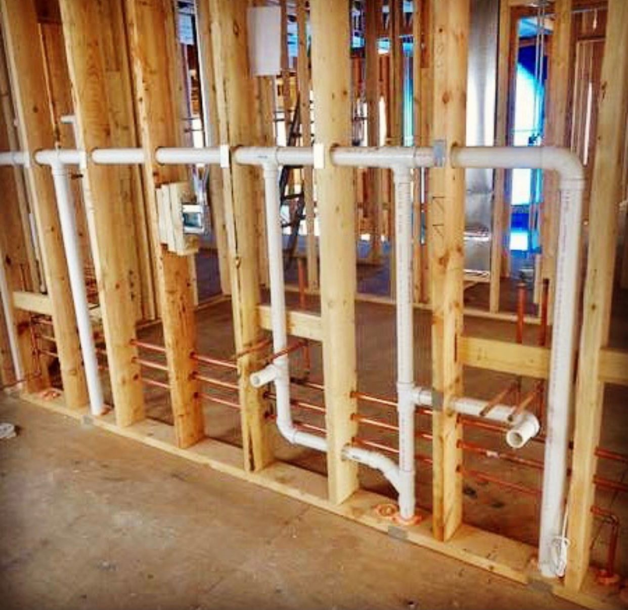 Rough-in plumbing with white PVC drain pipes and copper water supply lines installed within a wooden wall frame.
