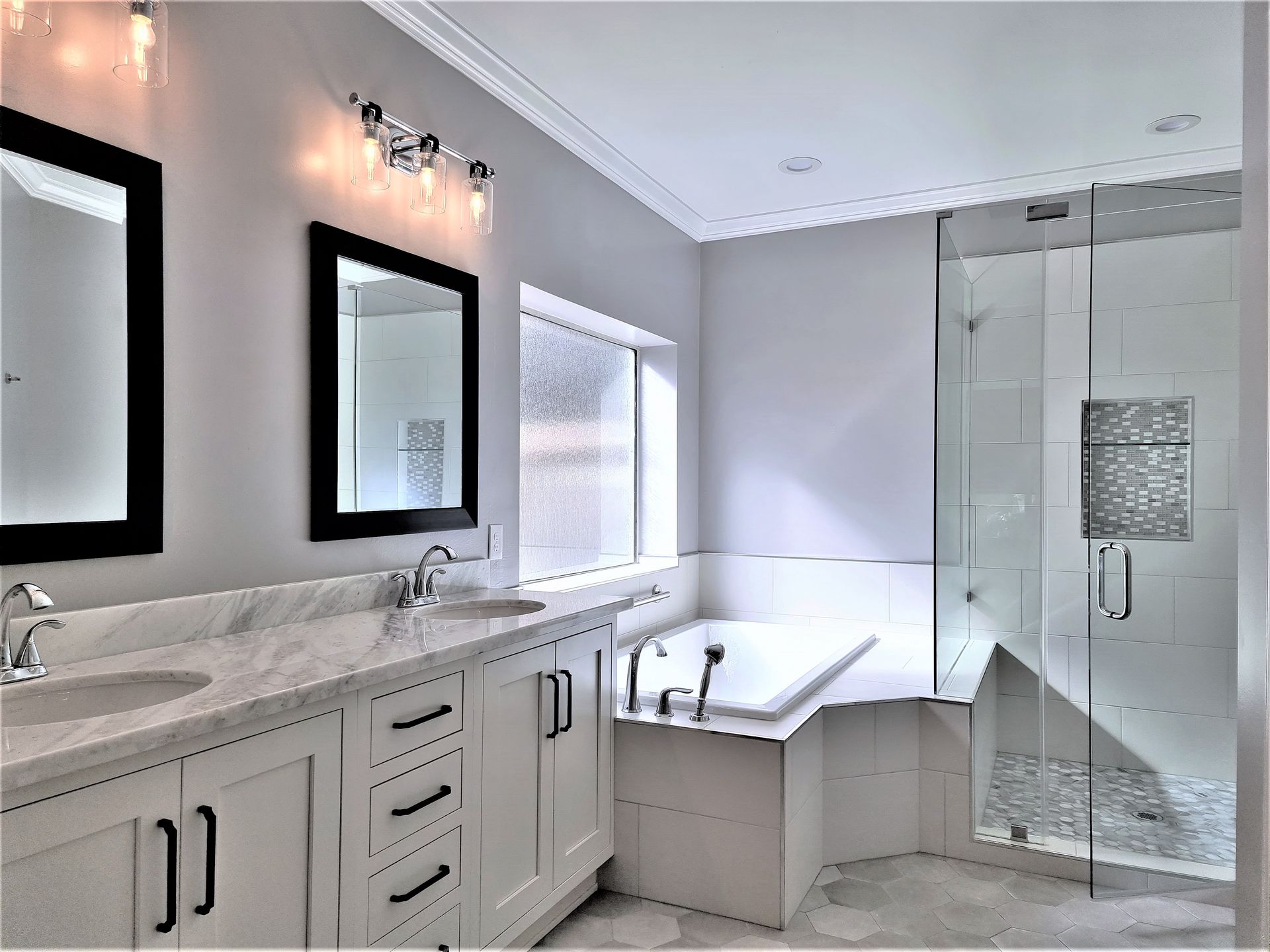 A modern bathroom featuring a white double vanity, two black-framed mirrors, a soaking tub, and a glass-enclosed shower.