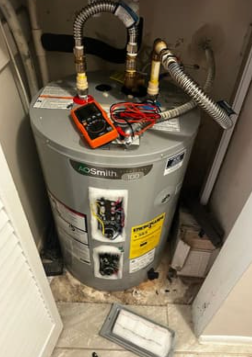 An A.O. Smith electric water heater in a closet with the access panels removed and a digital multimeter on top.