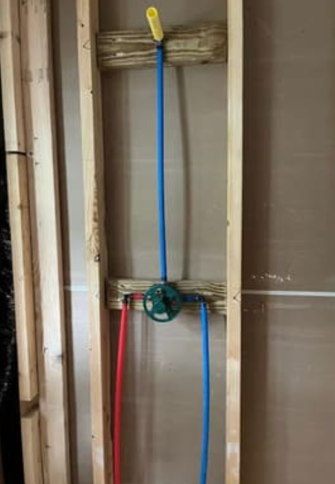 Plumbing rough-in for a shower, showing a valve with red and blue PEX pipes mounted between two wooden wall studs.