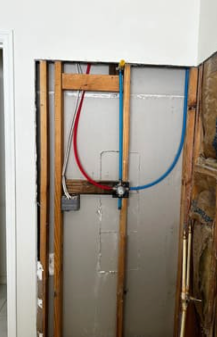 A view of a wall cavity showing exposed wooden studs, red and blue PEX plumbing pipes, and electrical wiring.