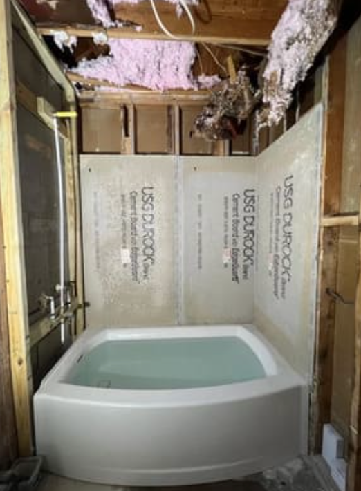 A bathtub installed in an unfinished bathroom with exposed wall studs, insulation, and USG Durock cement board walls.