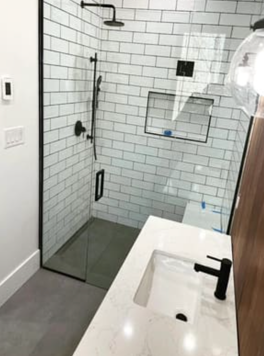 A modern bathroom featuring a white subway-tiled walk-in shower with black fixtures and a white vanity with a black faucet.