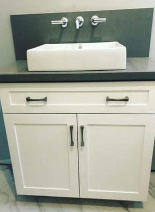 A white rectangular vessel sink with wall-mounted chrome fixtures on a dark gray countertop and white cabinet base.