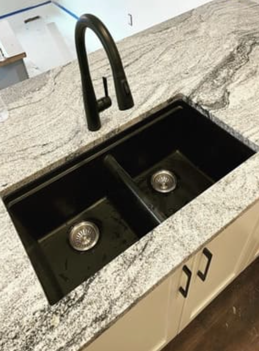A modern black double-basin kitchen sink with a high-arc faucet, set into a white and grey granite countertop.
