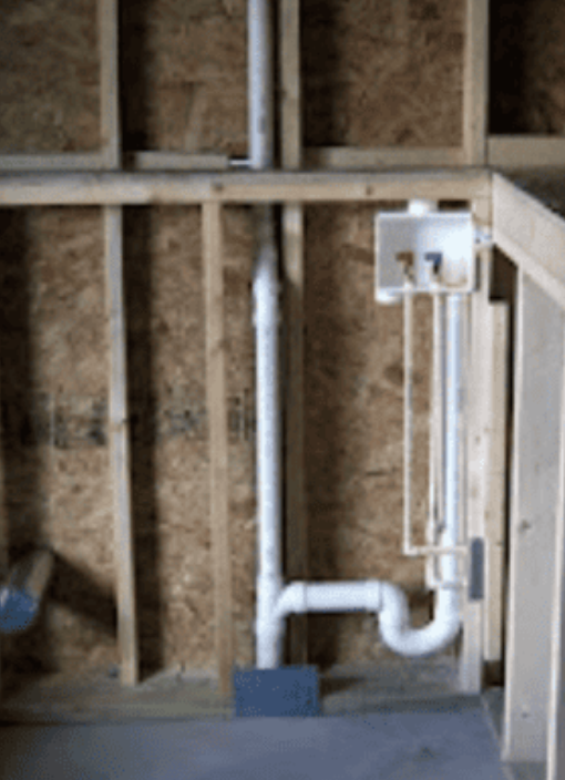 Unfinished wall framing with white PVC drain pipe, vent, and a laundry box with hot and cold water hookups.