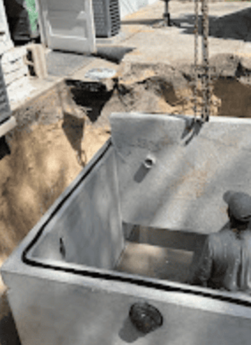 A construction worker stands inside a large, rectangular concrete structure lowered into an excavated site.