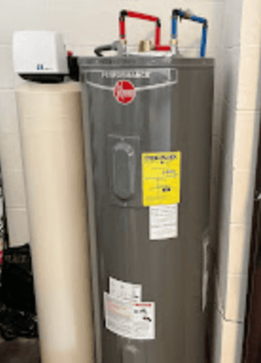 A Rheem Performance water heater stands next to a tall, tan water softener tank in a basement setting.