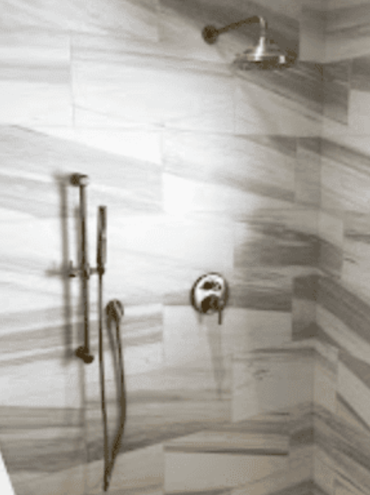 A tiled shower interior featuring a wall-mounted showerhead, a handheld shower wand on a slide bar, and a control handle.