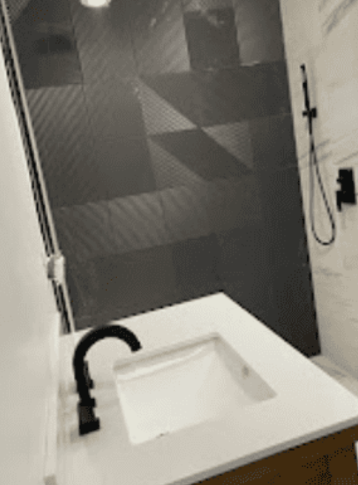 Modern bathroom vanity with a white countertop, black faucet, and a large-format gray tiled shower wall in the background.