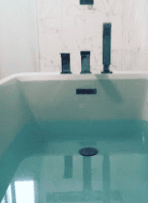 A filled bathtub with modern matte black hardware set against a light marble tiled wall.