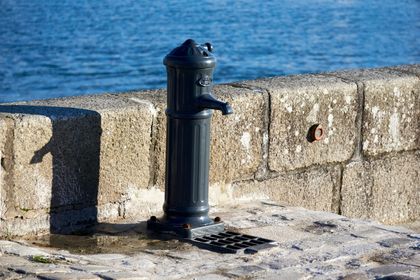 Black water fountain on a stone waterfront wall with blue sea in the background