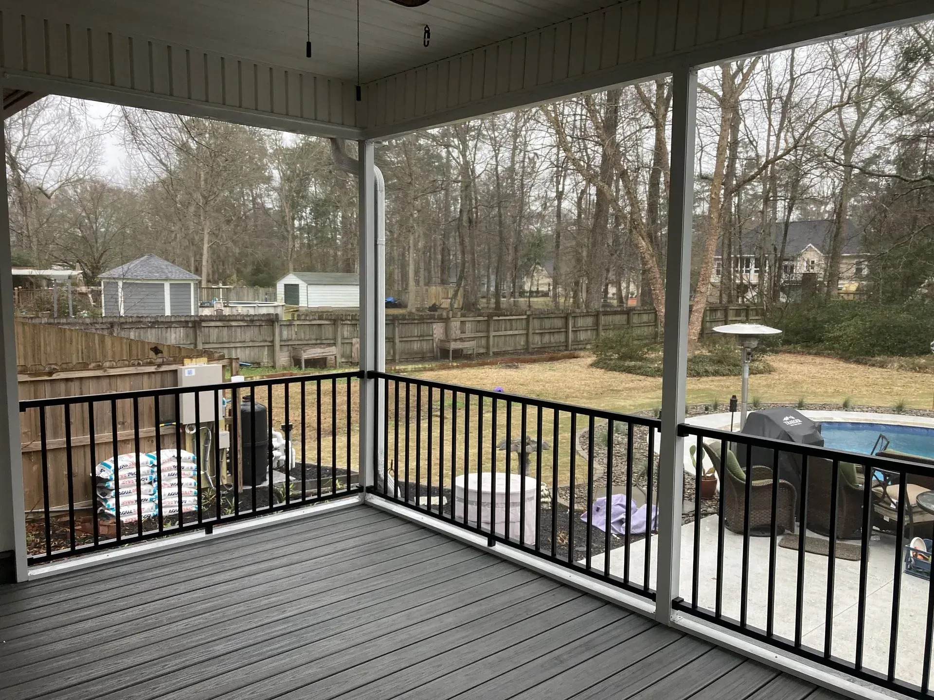 A screened in porch with a black railing overlooking a backyard and a pool.