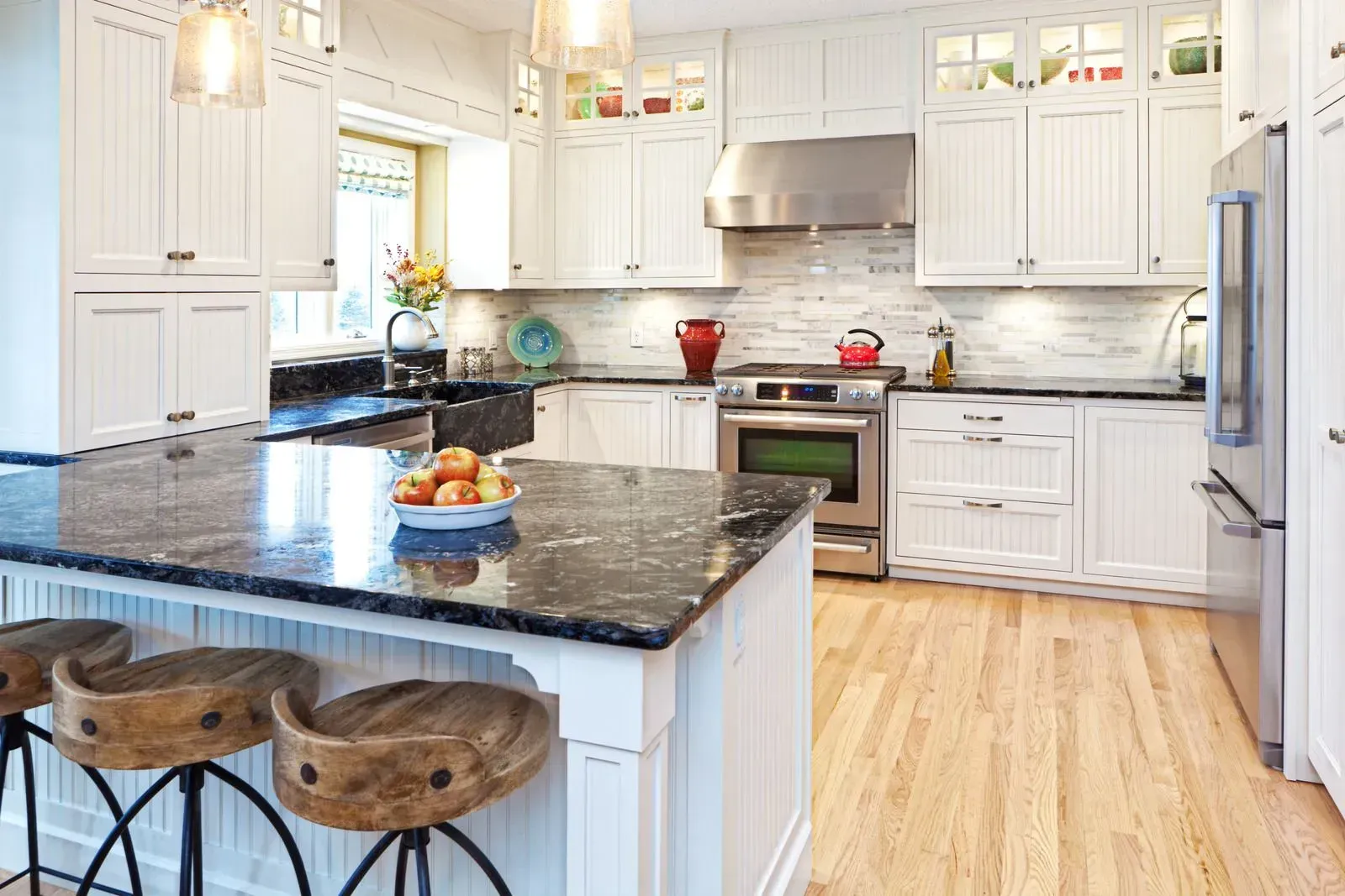 A kitchen with white cabinets , granite counter tops , stainless steel appliances and wooden floors.