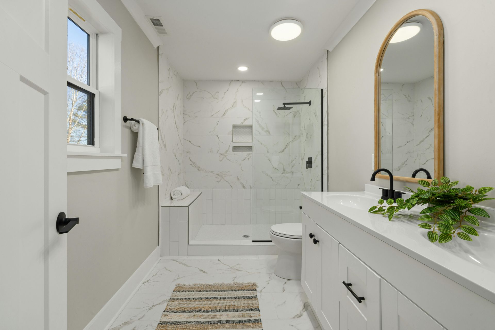 Bright white modern bathroom with marble tile, walk-in shower, vanity, and oval mirror