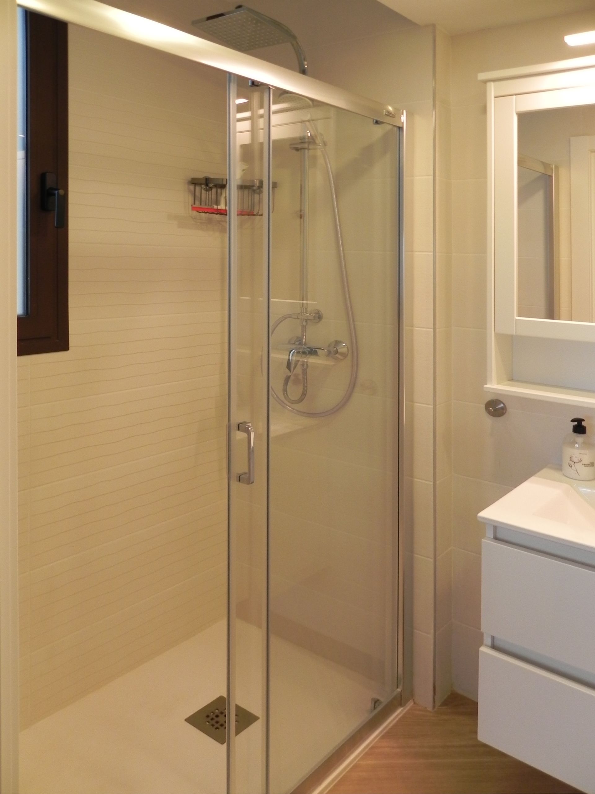 Shower with glass doors in a bathroom with white walls and a vanity.