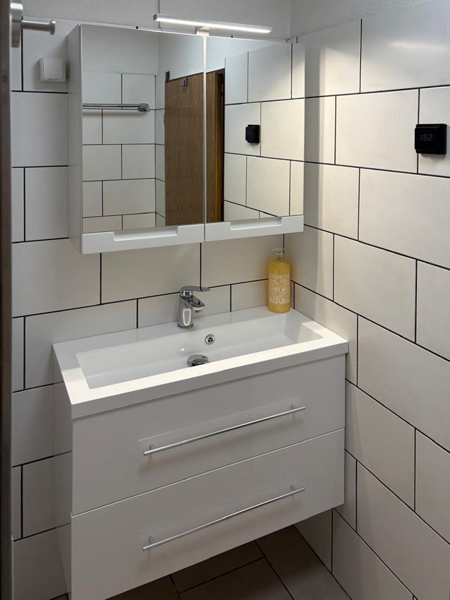 White bathroom vanity with two drawers, sink, and mirror with overhead light.